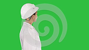 Young woman in hard hat walking and looking around on a Green Screen, Chroma Key.