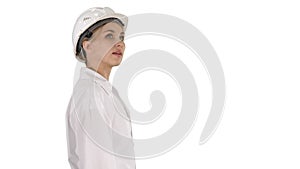 Young woman in hard hat walking and looking around on white background.