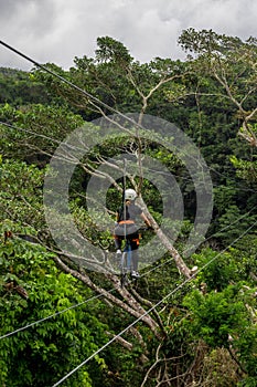 young woman with harness and helmet riding zipline bicycles surrounded by vegetation and a beautiful waterfall in Costa Rica