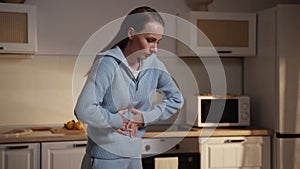 Young woman has a stomach ache at home. A woman in a blue sweater stands in the kitchen and holds her stomach in pain