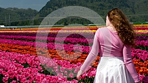 young woman has a white skirt pink jacket long blond hair against white tulips a red stripe in a field of tulips Girl in