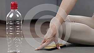 Young woman has workout at home during quarantine. Cut view and close up of woman`s hand taking smartphone from yoga mat