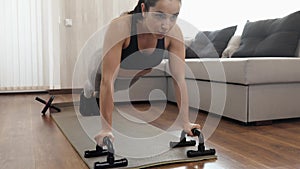 Young woman has workout at home during quarantine. Front voew of strong powerful female person doing push-ups with