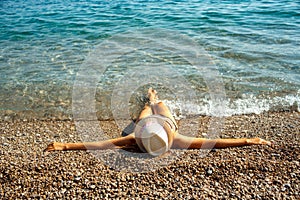 Young woman in a hat and bikini lying on the beach in hot summer