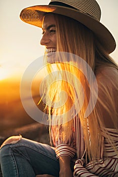 Young woman in hat is laughing against of sunset background.