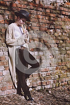 Young woman in a hat playing the flute in the street. Hipster girl outdoors