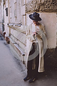 Young woman in a hat playing the flute in the street. Hipster girl outdoors