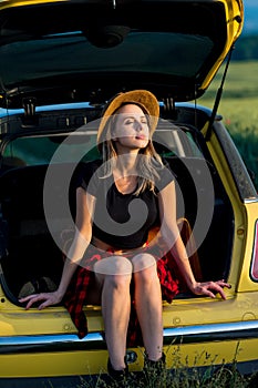 Young woman with hat sits in trunk of car