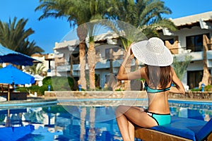 Young woman in hat sitting on a sun lounger near swimming pool, concept time to travel. Relax in the pool summer