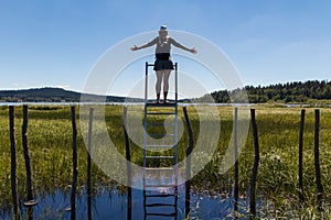 Young woman with hat standing on ladder on educational trail Olsina from back. Sumava reserve, Czech summer landscape