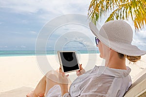 Young woman with hat using tablet with empty black screen on the beach. Girl Freelancer working