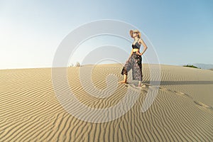 Young woman with hat walking in the desert dunes with footsteps in the sand during sunset