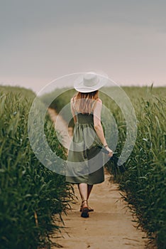 Young woman in a hat walking in a wheat field, enjoys life and summer. Wheat field.Healthy lifestyle Concept