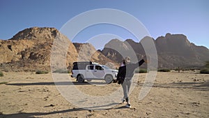 Young woman with hat walks to her car in desert. SUV off road auto.