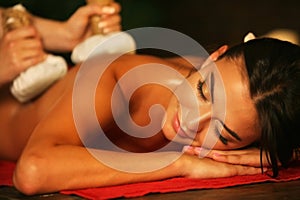 Young woman have hot poultice massage in spa salon.