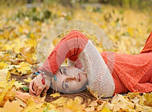 Young woman have a rest in autumn park, lay in yellow maple leaves, dressed in orange sweater