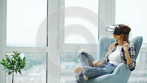Young woman have VR experience using virtual reality headset sitting in chair on balcony