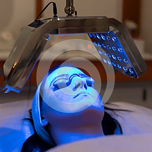 Young woman having blue LED light facial therapy treatment in beauty salon
