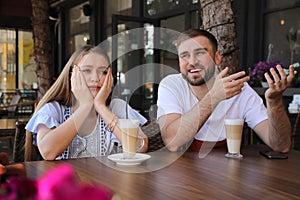 Young woman having boring date with talkative guy in outdoor cafe