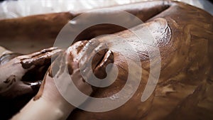 Young woman having chocolate applied on her back by beautician in a spa salon. Action. Details of relaxing body massage.