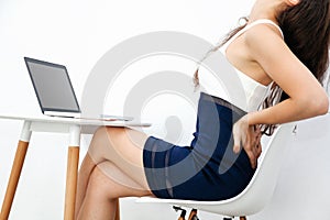 Young woman having chronic back pain / backache / office syndrome while working with laptop on white desk