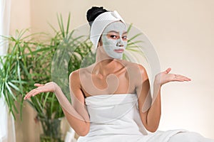 Young woman having clay facial mask in beauty salon