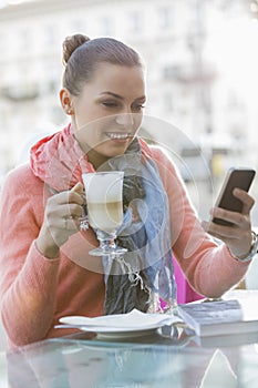 Young woman having coffee while using cell phone at sidewalk cafe