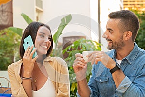 Young woman having a conversation on smartphone sitting next to her boyfriend in an outdoor