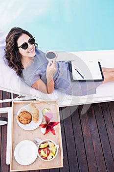 Young woman having cup of tea near poolside