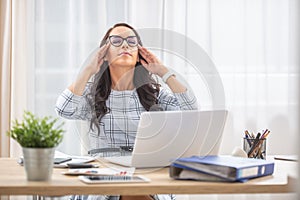 Young woman having eyes closed, fingers on her temples, retrieving mental energy in her work-life balance