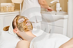 Young woman having face treatment in spa salon, facial scrub for face