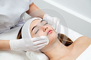 Young woman having facial beauty treatment. Beautician cleaning and touching female face with cotton pad or sponge