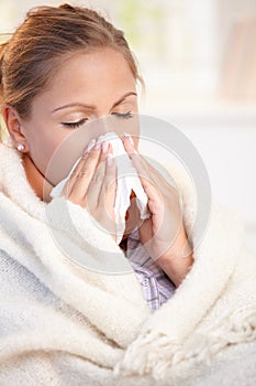 Young woman having flu blowing her nose