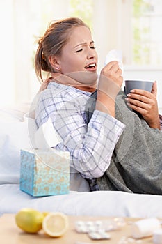 Young woman having flu laying in bed sneezing