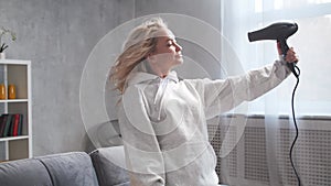 Young woman having fun and dancing, drying her hair with a hairdryer at home.