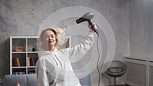 Young woman having fun and dancing, drying her hair with a hairdryer at home.