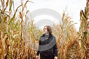 Young woman having fun on pumpkin fair at autumn. Person walking among the dried corn stalks in a corn maze.