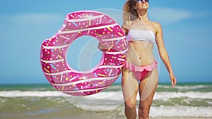 Young woman having fun with toy Inflatable ring donut on the beach.