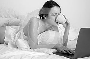 Young woman having good time in bed on the living room with coffee and laptop.