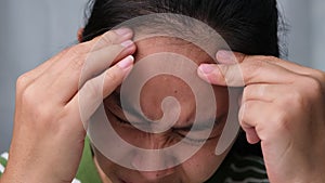Young woman having headache against white curtain background in room.