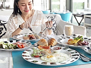 Young woman having healthy breakfast - fried egg, beans, salad, tomatoes, mushrooms, bacon and toast