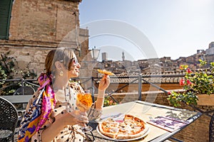 Young woman having lunch with pizza and wine at outdoor restaurant in Siena town