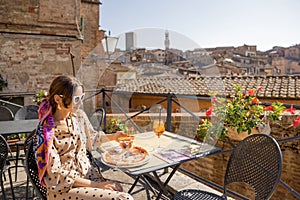 Young woman having lunch with pizza and wine at outdoor restaurant in Siena town