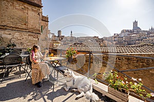 Young woman having lunch, sitting with a dog at outdoor restaurant in Siena town