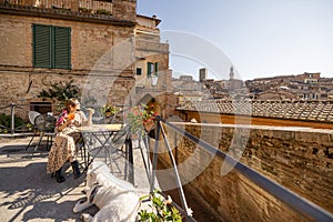 Young woman having lunch, sitting with a dog at outdoor restaurant in Siena town