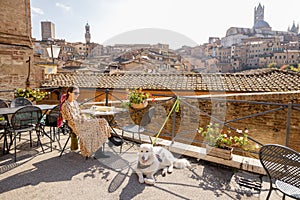 Young woman having lunch, sitting with a dog at outdoor restaurant in Siena town