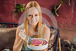 Young woman having a mediterranean breakfast seated at her sofa and eats Healthy tropical breakfast, smoothie bowl with