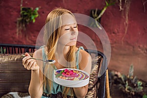 Young woman having a mediterranean breakfast seated at her sofa and eats Healthy tropical breakfast, smoothie bowl with