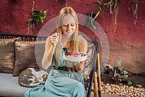 Young woman having a mediterranean breakfast seated at her sofa and eats Healthy tropical breakfast, smoothie bowl with