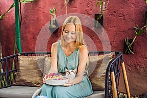 Young woman having a mediterranean breakfast seated at her sofa and with her cat and eats Healthy tropical breakfast